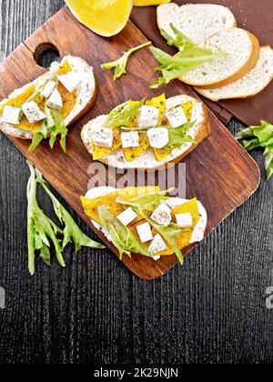 Bruschetta mit Kürbis und Rucola auf dunklem Brett Stockfoto