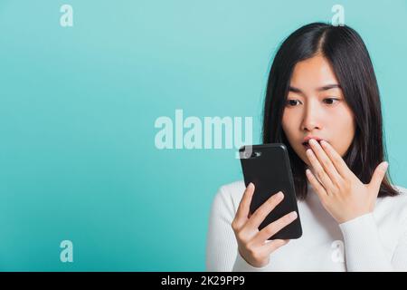 Frau überrascht schockiert mit Handy schließen Mund mit Handfläche Stockfoto