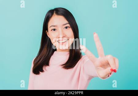 Junge asiatische, schöne lächelnde Frau tragen kiefergerecht geformte Silikon-Zahnhalter auf den Zähnen, die V-Zeichen zeigen, Siegesfinger isoliert auf blauem Hintergrund, nach abnehmbaren Zahnspangen. Zahnhygienisches Konzept Stockfoto