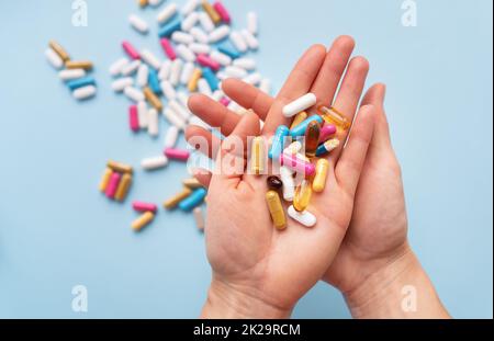 Das Mädchen hält in ihren Händen viele bunte, helle Pillen. Blauer Hintergrund, Platz für eine Inschrift. Medizinische Konzepte und Gesundheit. Stockfoto