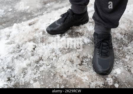 Ein Mann in winterlichen wasserdichten Turnschuhen steht auf einer eisigen Straße, Schuhe für winterliche Spaziergänge. Geht unter freiem Himmel. Stockfoto