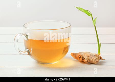 Transparente Tasse mit heißem Tee, nass von Dampf auf Glas, chemische Ingwerwurzel mit Grün sprießen. Stockfoto