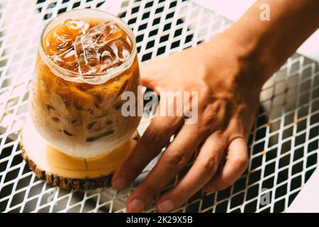 Hand halten Eis Latte Kaffee in einem Glas mit Creme auf dem Boden. Kalten Sommer trinken Hintergrund Stockfoto