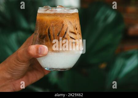 Hand halten Eis Latte Kaffee in einem Glas mit Creme auf dem Boden. Kalten Sommer trinken Hintergrund Stockfoto