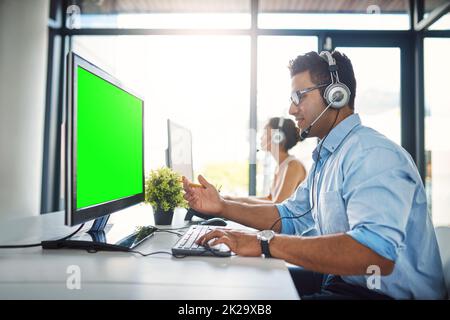 Hes der Mann für den Job. Ausgeschnittene Aufnahme eines hübschen jungen Mannes, der in einem Callcenter mit einer Kollegin im Hintergrund arbeitet. Stockfoto