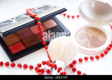 Weißes Gesichtspulver und Bronzer, schwarze Verpackung mit einer Schattenbürste und auf weißem Hintergrund liegend, Geflecht mit roten Perlen Nahtaufnahme Stockfoto