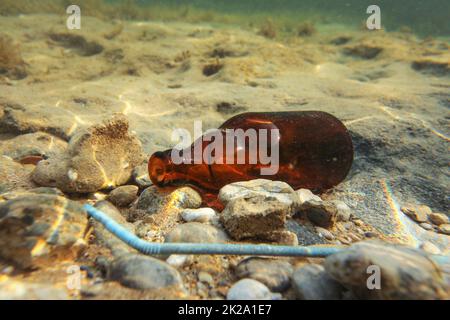 Kleine braune Bier Flasche und Kunststoff blau Stroh auf sandigen Meeresgrund. Unterwasser Foto, ocean Konzept littering. Stockfoto