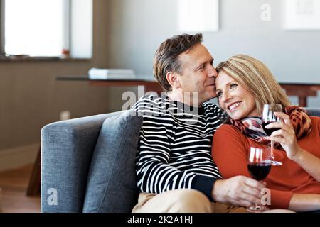 Sie lieben ein wenig Romantik Aufnahme eines lächelnden, reifen Paares, das auf ihrem Sofa sitzt und Wein trinkt. Stockfoto