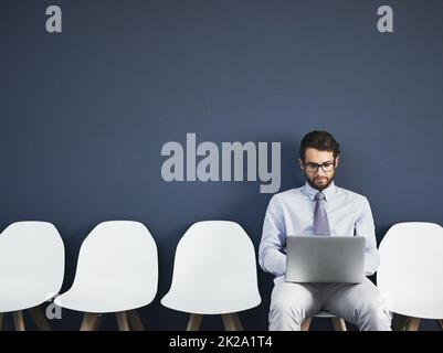 Er kam vorbereitet. Studioaufnahme eines jungen Geschäftsmannes, der einen Laptop benutzt, während er vor grauem Hintergrund in der Schlange wartet. Stockfoto