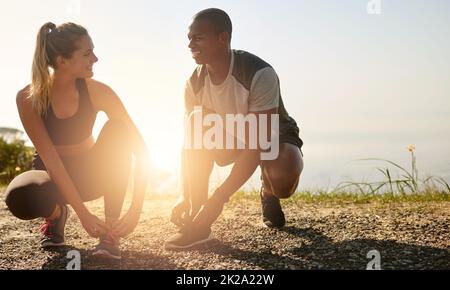 Schnappen Sie sich Ihren Workout-Freund und los geht's. Aufnahme eines fetten jungen Paares, das sich vor einem Lauf im Freien die Schnürsenkel schnürt. Stockfoto