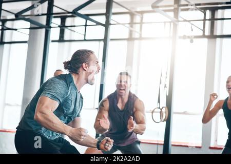 Verwandeln Sie Ihre Träume in die Realität. Aufnahme einer Fitnessgruppe, die einen Sieg im Fitnessstudio feiert. Stockfoto