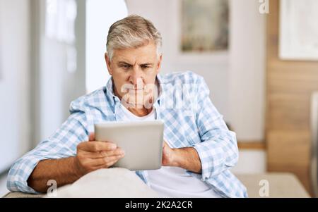 Blättern durch Websites. Aufnahme eines reifen Mannes, der sein digitales Tablet benutzt, während er sich zu Hause auf seinem Sofa entspannt. Stockfoto