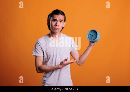 Junger asiatischer Mann, der zu spät läuft, mit Retro-Alarm, Pünktlichkeit, Terminplan, Zeitmanagement-Konzept. Person schlief am Morgen, ängstlicher Teenager zeigte auf Vintage-Uhr Stockfoto