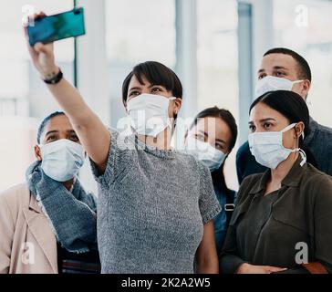 Eine neue Normalität annehmen. Aufnahme einer Gruppe junger Menschen, die Masken tragen und Selfies am Flughafen machen. Stockfoto