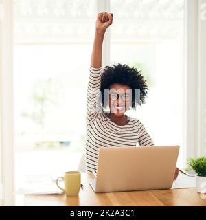 Der Erfolg ist ihr für die Einnahme. Porträt einer jungen Frau, die zu Hause an ihrem Laptop arbeitet und eine Faustpumpe macht. Stockfoto