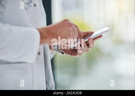 Es ist eine Möglichkeit, Patienten auf dem Laufenden zu halten. Nahaufnahme eines unverkennbaren Arztes, der auf seinem Handy SMS schreibt. Stockfoto