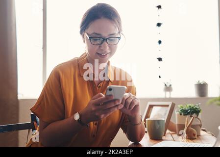 Willkommen im digitalen Zeitalter. Eine kurze Aufnahme einer attraktiven jungen Geschäftsfrau, die allein in ihrem Heimbüro sitzt und auf ihrem Handy schreibt. Stockfoto