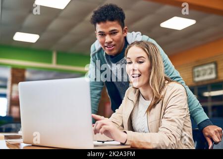 Hier finden Sie alle Informationen auf Knopfdruck. Aufnahme eines jungen Mannes, der anschaut, während eine Studentin an einem Laptop arbeitet. Stockfoto