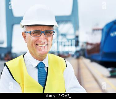 Lächelnder Meeresbeobachter. Porträt eines Hafenarbeiters, der inmitten der Schifffahrt am Hafen steht. Stockfoto