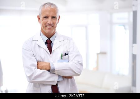 Ihre Gesundheit ist meine oberste Priorität. Porträt eines reifen Arztes, der mit gekreuzten Armen steht. Stockfoto