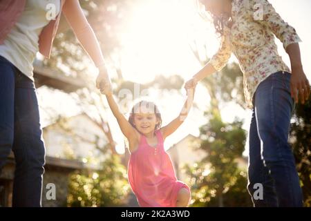 Viel Spaß mit ihrer Familie. Ein süßes kleines Mädchen, das von ihrer Mutter und Großmutter im Garten geschwungen wird. Stockfoto