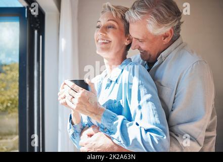 Liebe, Seniorenpaar und Urlaub im Ruhestand, während wir uns umarmen, Kaffee trinken und zu Hause oder im Hotel aus dem Fenster schauen. Glücklicher reifer Mann und Stockfoto