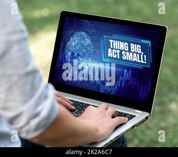 Schild mit der Aufschrift "Ding Big, Act Small". Das Konzeptfoto beginnt kurzfristig, um ein lebenslanges Ziel zu erreichen Frau, die auf einem Laptop tippt, sitzt draußen hinter der Rückansicht und arbeitet von zu Hause aus. Stockfoto