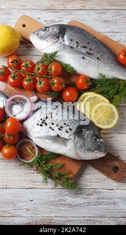 Roher, frischer, ungekochte dorado- oder Brassen-Fisch mit Zitrone, Kräutern, Kirschtomaten und Gewürzen auf schwarzem Hintergrund Stockfoto