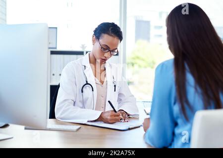 Ich werde eine Empfehlung für Sie schreiben. Aufnahme einer jungen Ärztin, die in ihrem Sprechzimmer mit einer Patientin ein Gespräch führt. Stockfoto