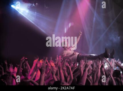 Surfen auf einer Welle des Lobes. Ein Stage Diver wird bei einem Rockkonzert über das Publikum getragen. Stockfoto