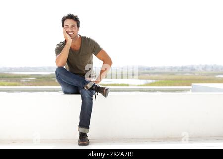 Lässig und unbeschwert. Porträt eines hübschen jungen Mannes, der nachdenklich aussieht, während er draußen sitzt. Stockfoto