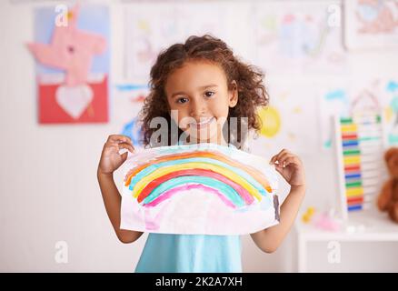 Sie lieben nicht nur die Farben. Aufnahme eines kleinen Mädchens, das ein Bild von einem Regenbogen hochhält. Stockfoto