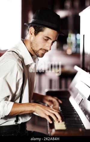 Die Musik aus dem tiefsten Inneren seiner Seele auszudrücken. Ein hübscher junger Mann, der in einem Club Klavier spielt. Stockfoto