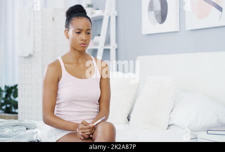 Was in aller Welt soll ich jetzt tun? Aufnahme einer attraktiven jungen Frau, die sich Sorgen macht, während sie sich die Ergebnisse ihres Schwangerschaftstests in ihrem Schlafzimmer zuhause ansieht. Stockfoto