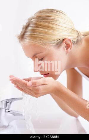 Erhaltung einer gesunden und schönen Haut. Aufnahme einer attraktiven jungen Frau, die ihr Gesicht über einem Waschbecken mit Wasser wäscht. Stockfoto