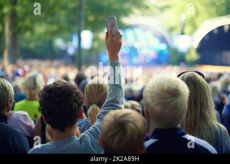 Halten Sie den Moment fest. Aufnahme eines Mitglieds der Menge, das mit seinem Kameratelefon ein Foto auf einem Musikfestival machte. Stockfoto