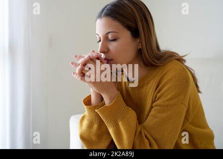 Spiritualität und junge Menschen. Mädchen, das zu Hause allein betet. Besorgte Frau, die während der russischen Invasion in der Ukraine um Stärke betet. Stockfoto