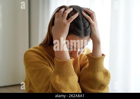 Psychische Gesundheit. Trauriges Mädchen, das auf dem Boden sitzt, mit den Händen im Haar frustriert. Stockfoto