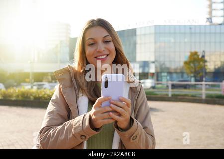 Lächelndes Mädchen in Winterkleidung mit Telefon in der Stadt Stockfoto