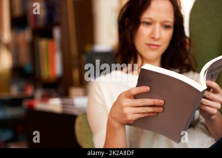 Eingetaucht in die Worte. Eine junge Frau liest ruhig ein Buch, während sie auf einem Stuhl sitzt. Stockfoto