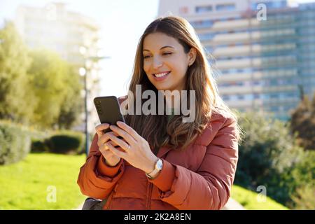 Portrait von Mädchen im Freien mit Smartphone trägt Wintermantel beobachten Video-Streaming Stockfoto