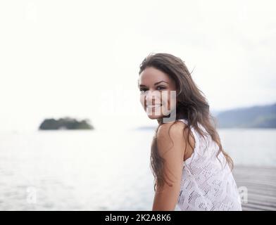 Sich die Zeit nehmen, um sich auf mich zu konzentrieren. Porträt einer attraktiven jungen Frau, die auf einem Steg am See sitzt. Stockfoto