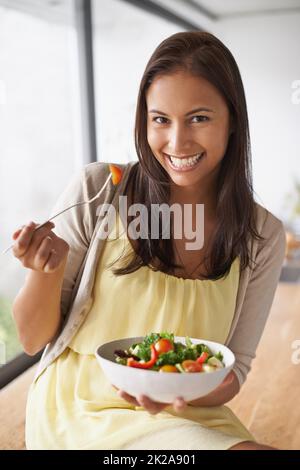 Genießen Sie einen gesunden Snack. Eine schöne junge Frau, die einen gesunden Salat genießt. Stockfoto