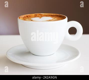 Der einzige Start in den Morgen. Aufnahme eines frisch zubereiteten Cappuccinos auf einem weißen Tisch. Stockfoto