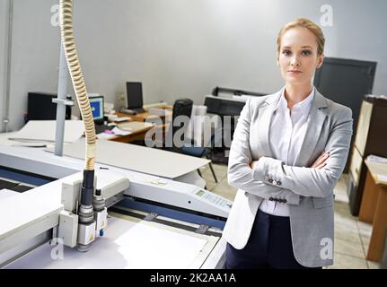 Lassen Sie uns drucken. Porträt eines jungen Vertrauten, der neben einer Druckmaschine steht. Stockfoto