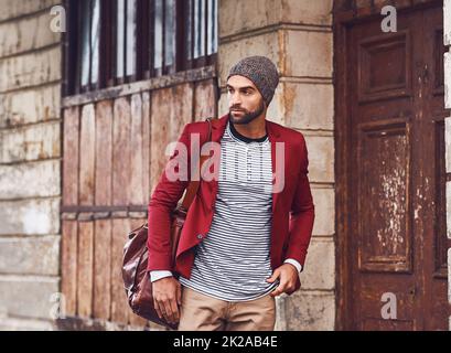 Immer in Bewegung mit Stil. Ein hübscher junger Mann mit roter Jacke, der in der Tasche auf der Straße spazieren geht. Stockfoto