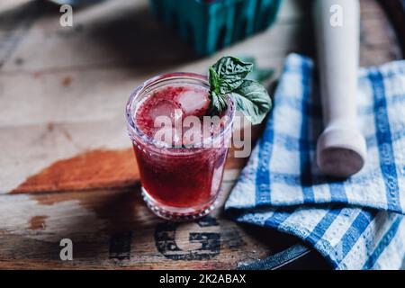 Cocktail-Drink aus Erdbeerbasil auf Fass mit blauer Gingham-Serviette und Holzschlamdler Stockfoto