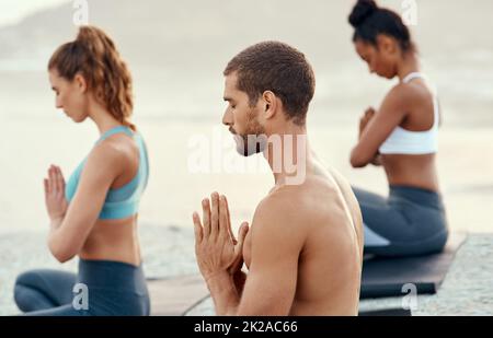 Nehmen Sie sich den Moment, um anwesend zu sein und in Frieden zu sein. Aufnahme einer Gruppe junger Menschen, die gemeinsam im Freien Yoga praktizieren. Stockfoto