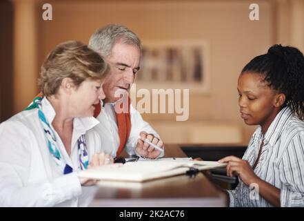 Freundliche Unterstützung an der Rezeption. Ein Seniorenpaar füllt Formulare an der Rezeption aus. Stockfoto