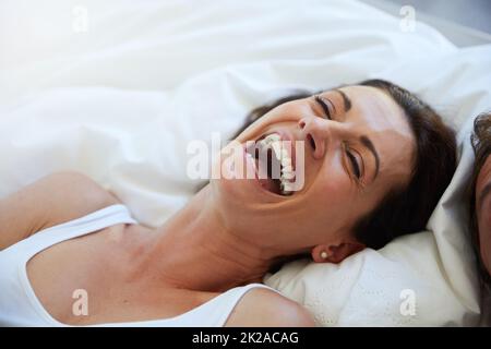 Nichts Besseres als Lachen, um die Stimmung zu heben. Aufnahme einer lachenden Frau, die sich im Bett neben ihrem Mann entspannt. Stockfoto